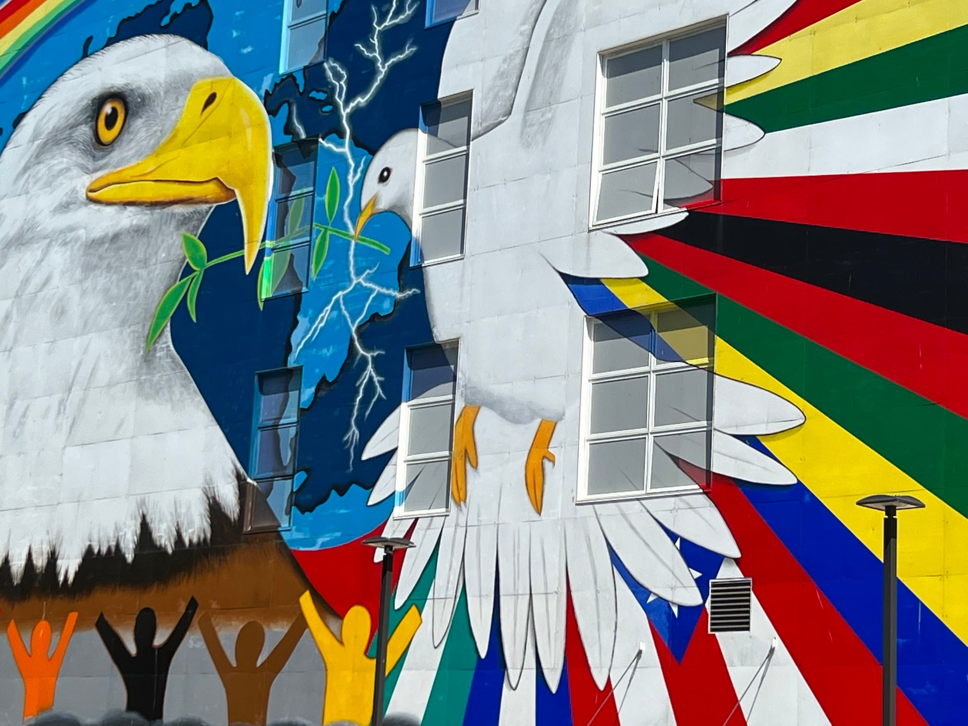 massive mural of bald eagle facing a dove with an olive branch, a globe backdrop, and multicolored stick figures holding their arms up in celebration.